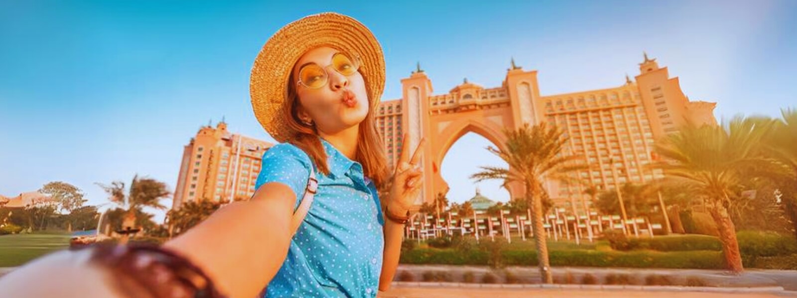Woman smiling, taking selfie in front of Atlantis Hotel during Dubai city tour, with palm trees in background.