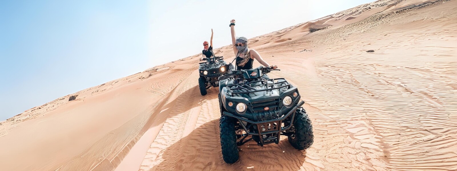 Two people riding quad bikes on a desert sand dune, enjoying an adventurous ride in the vast expanse.