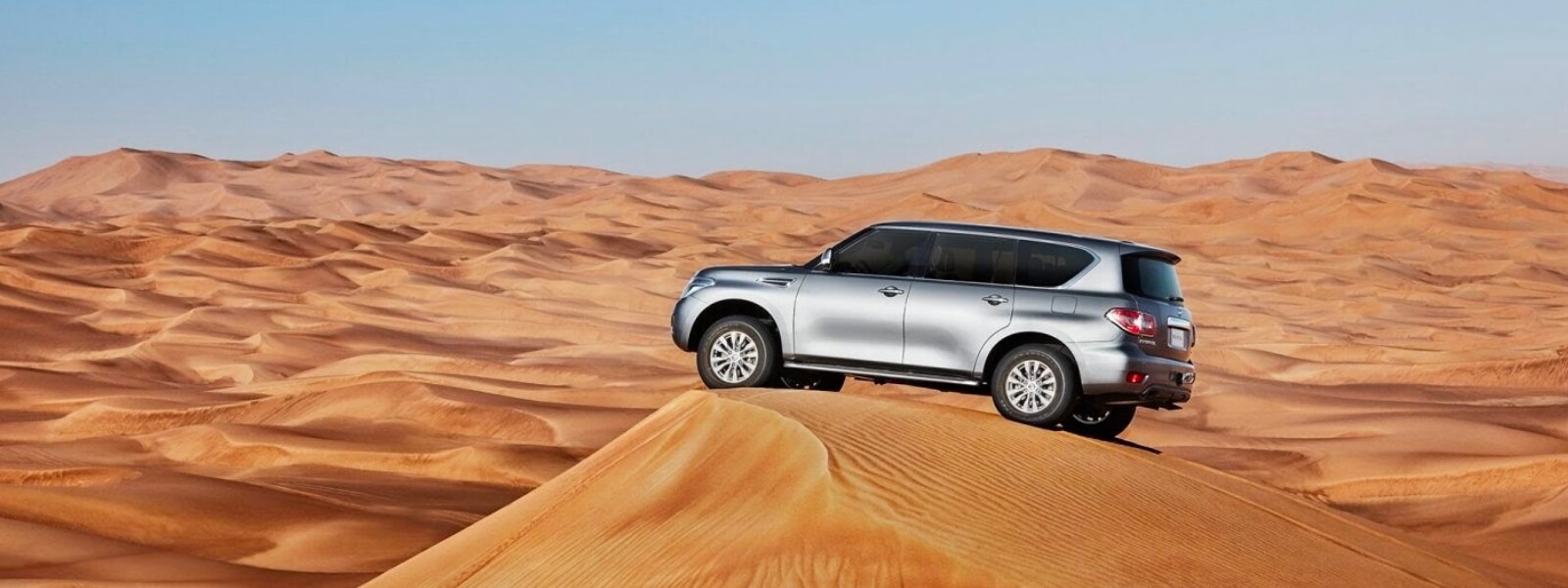 An SUV is parked on the top of the desert dune.