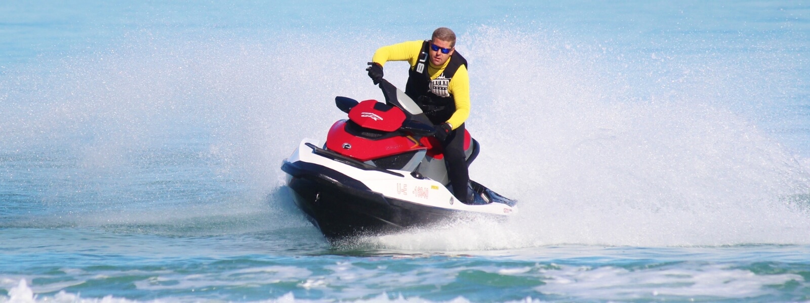 A man in a yellow and black jacket rides a jet ski against a mesmerizing city skyline, creating a captivating scene.
