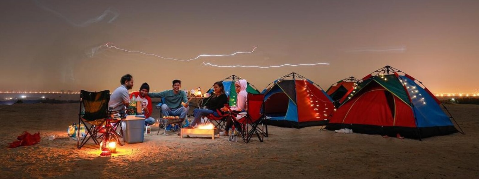 A group of people sitting around a campfire in overnight desert safari, enjoying the warmth and glow of the flames.