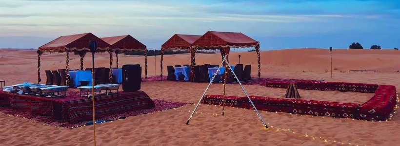 A private desert setup with tents and tables for an outdoor gathering in a serene desert setting.
