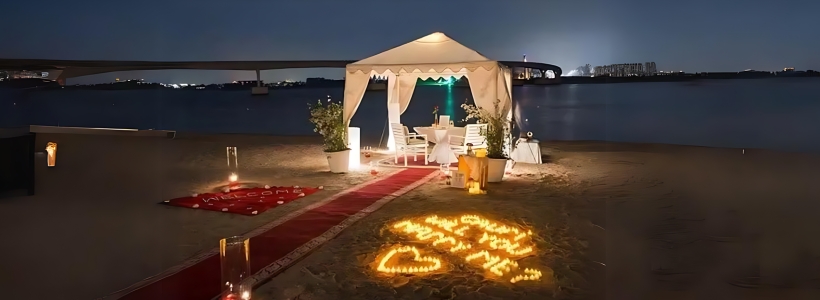 A romantic beach dinner setup in Dubai with white chairs, a floral arch, and the ocean in the background.