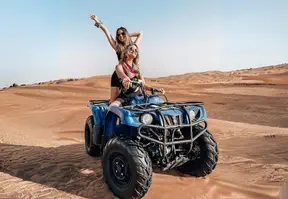 Two women riding on an ATV in the desert under the clear blue sky.