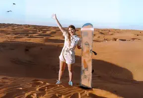 Woman confidently stands in desert holding sandboard, ready for adventurous ride.