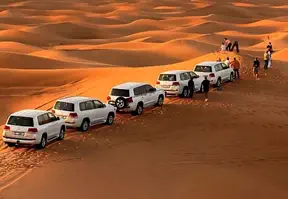 Five white cars parked in the desert with people standing beside them.