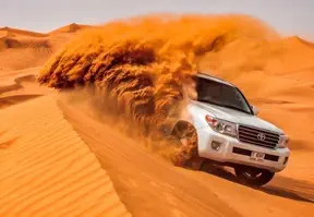 A white SUV conquering desert terrain, showcasing dune bashing with sand blowing in the background.