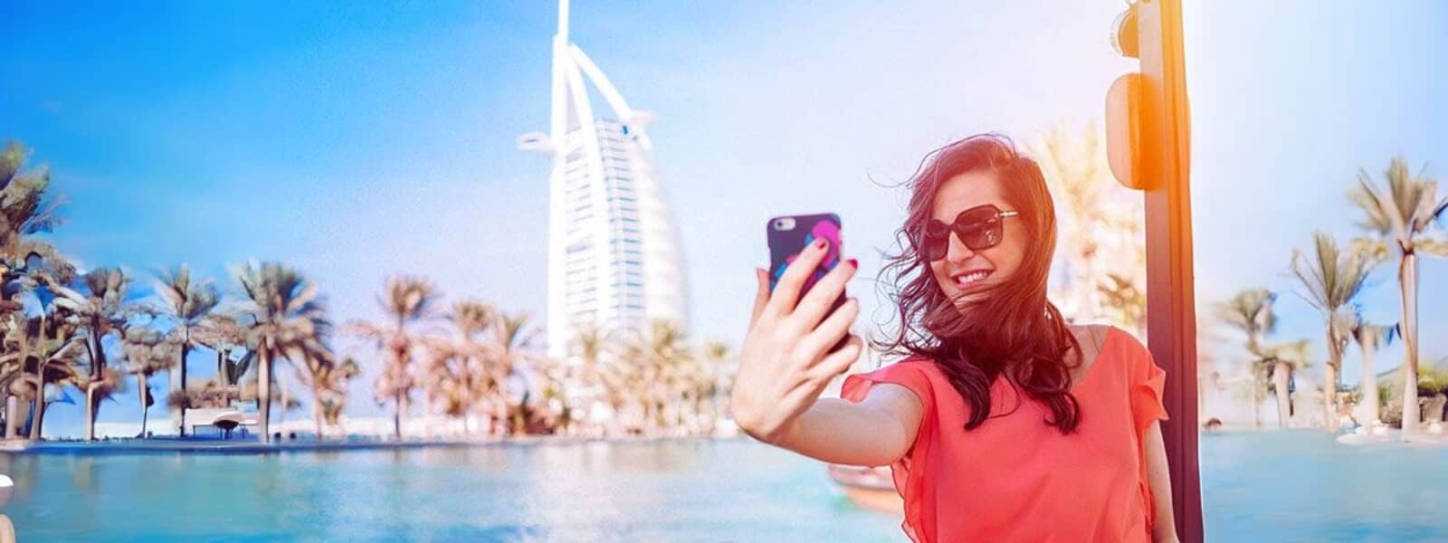 A woman taking a selfie with Burj Al Arab in the background during a Dubai city tour, highlighting the iconic landmark's grandeur.