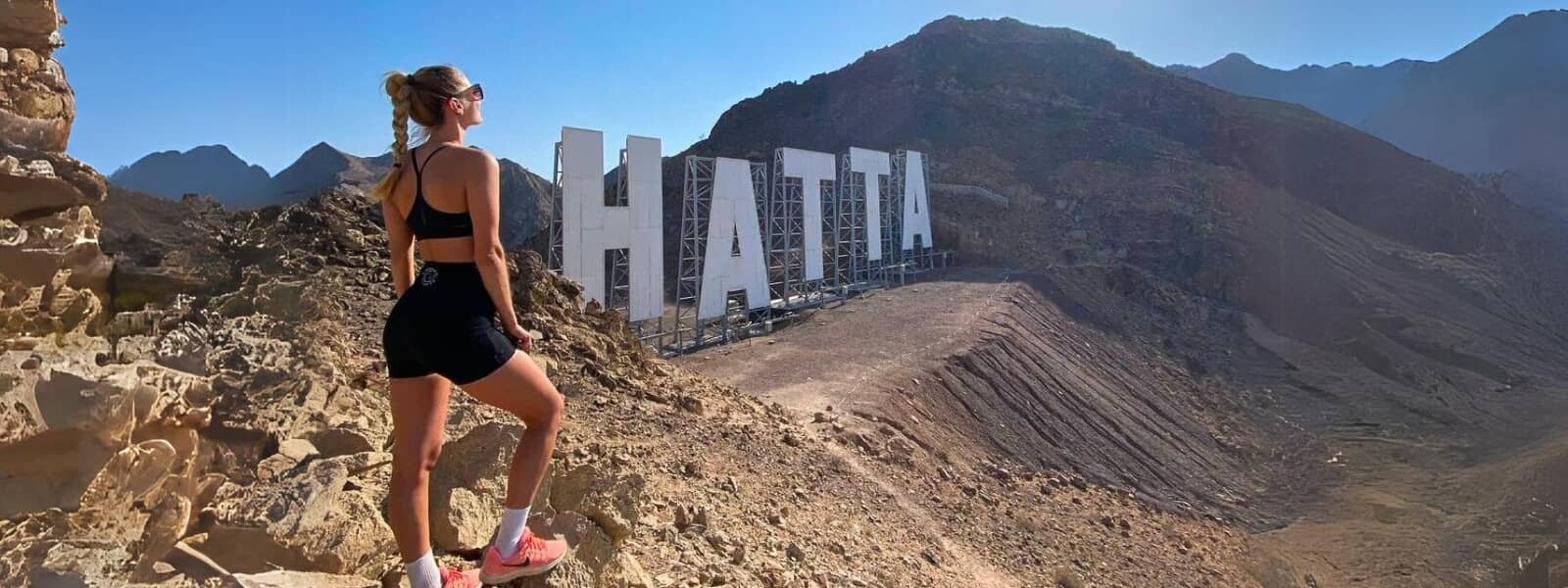 A woman triumphantly stands atop a mountain, with the word Hatta written nearby.