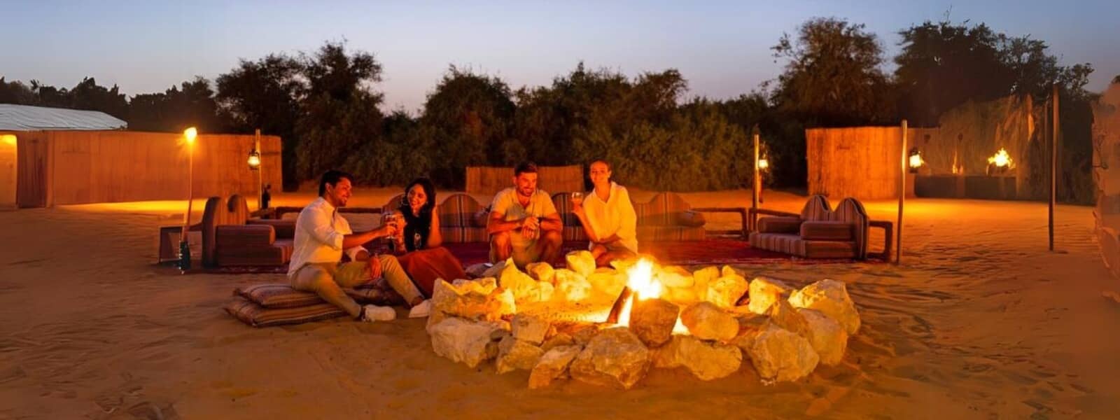 Four people sitting around a fire pit in the desert, enjoying the warmth and camaraderie amidst the vast, sandy landscape.