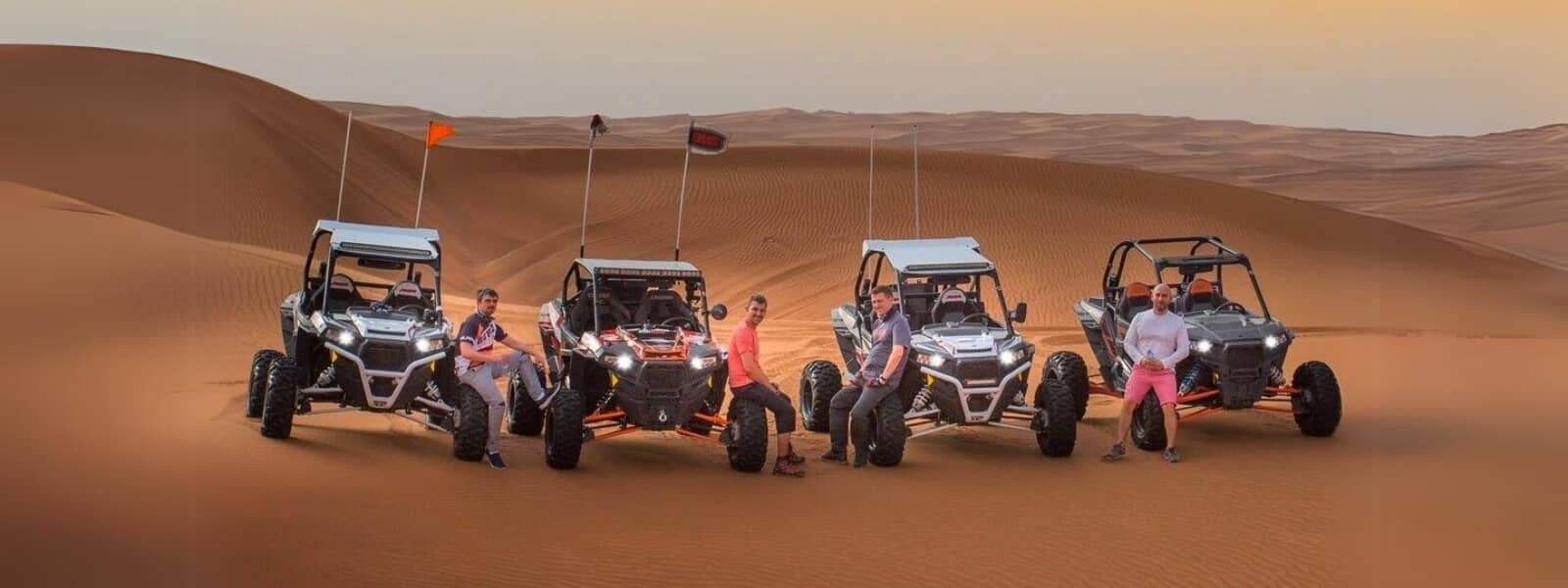 Four people riding dune buggies in the Dubai desert, enjoying an adventurous ride on their four-wheelers.