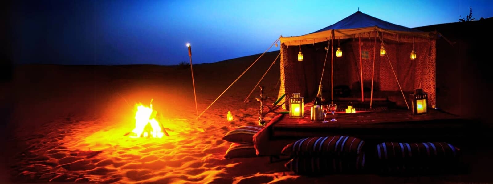 Desert camping scene with tent and bonfire at night.