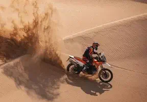 A person riding a motorcycle on a desert sand dune.