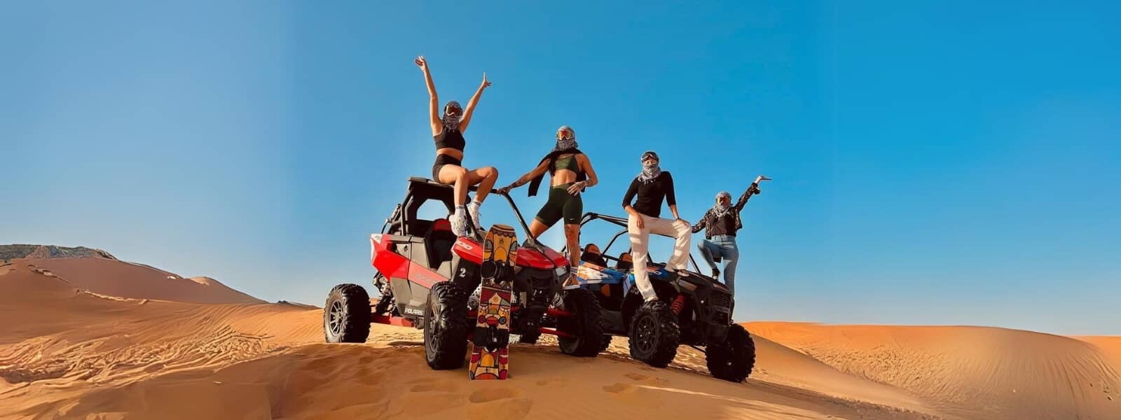 Four individuals riding dune buggies in the desert on a sunny day.