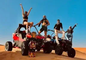 Four people riding four wheelers in the desert under a clear blue sky.
