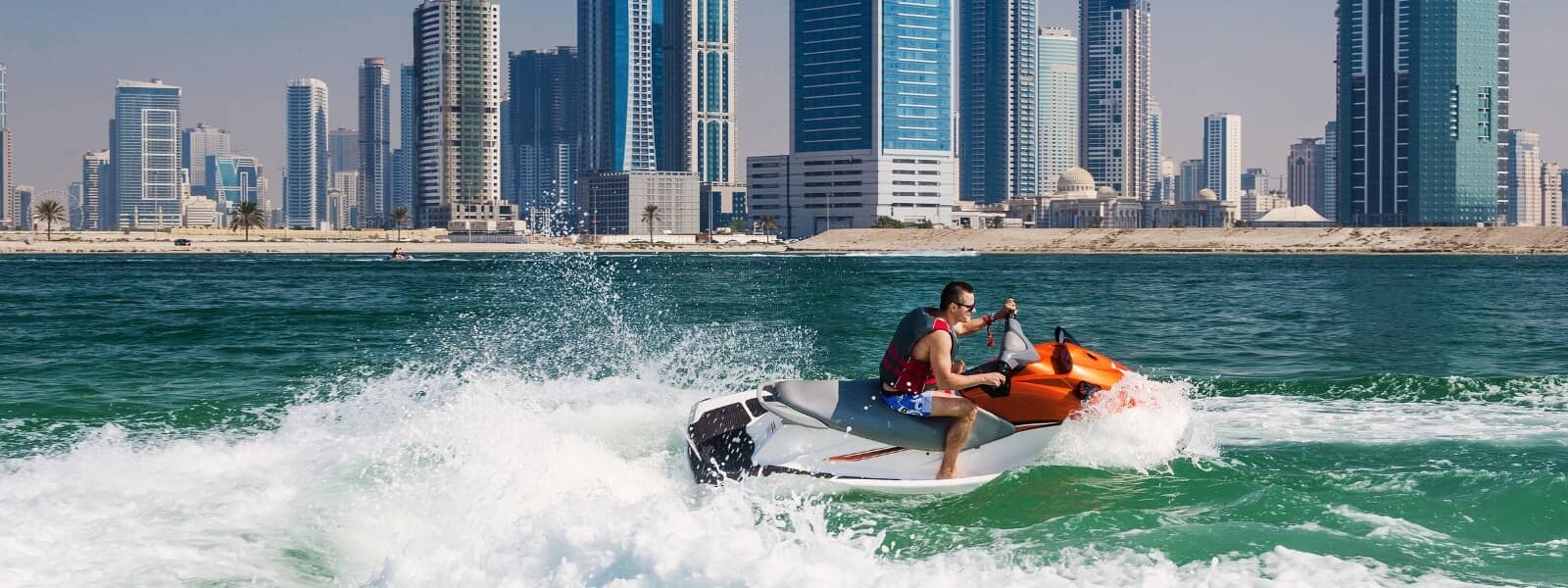 An individual enjoying a thrilling ride on a jet ski on the vast beach of Sharjah.